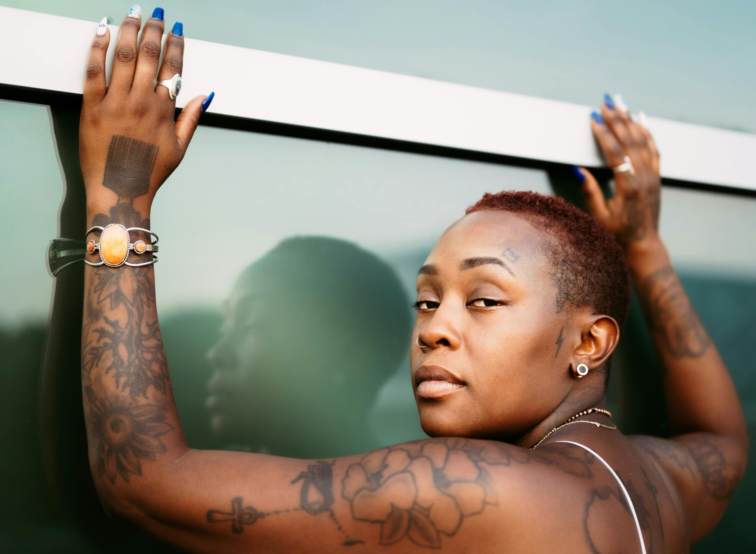 A bold portrait of a tattooed black woman with short hair and jewelry, showcasing her unique style.