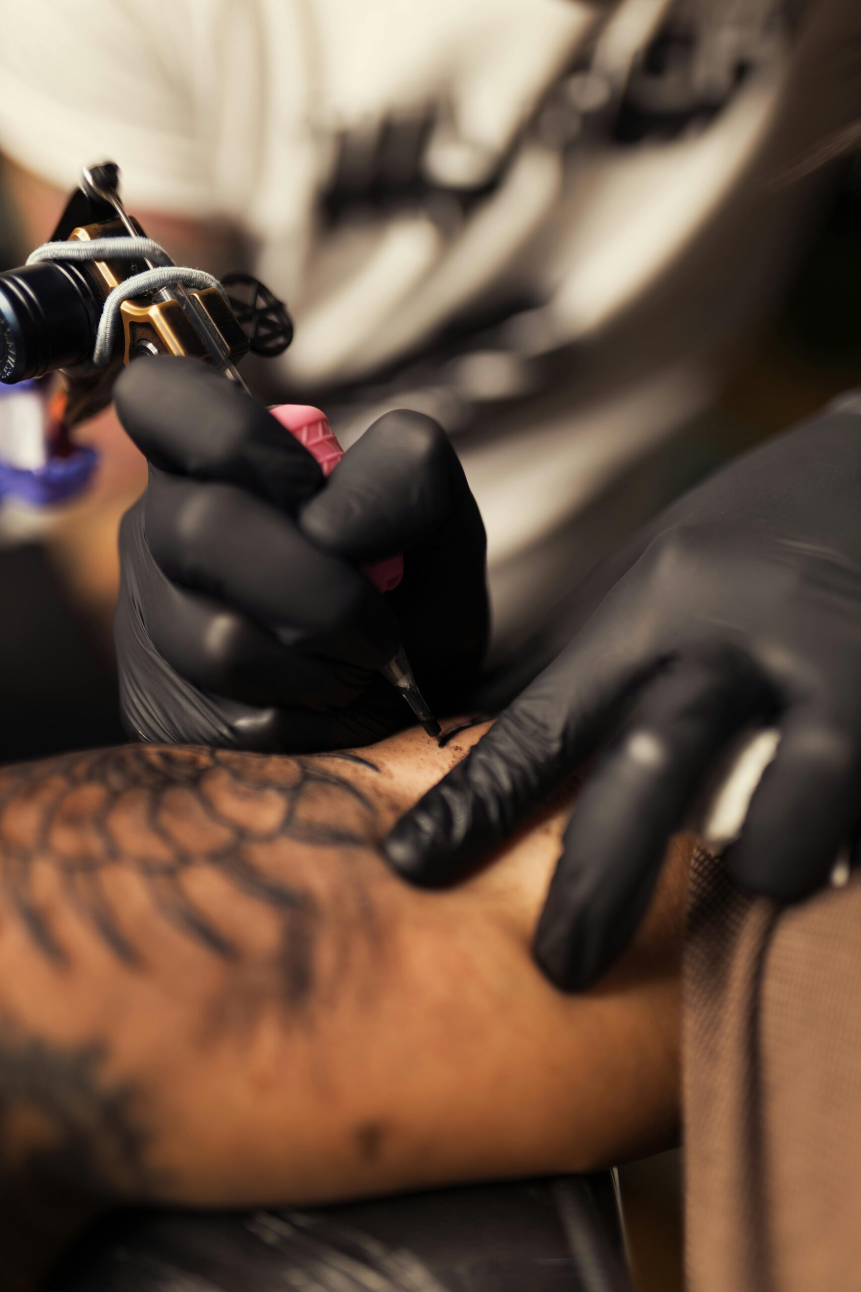 Close-up of a tattoo artist creating detailed artwork on a client's arm with black ink.
