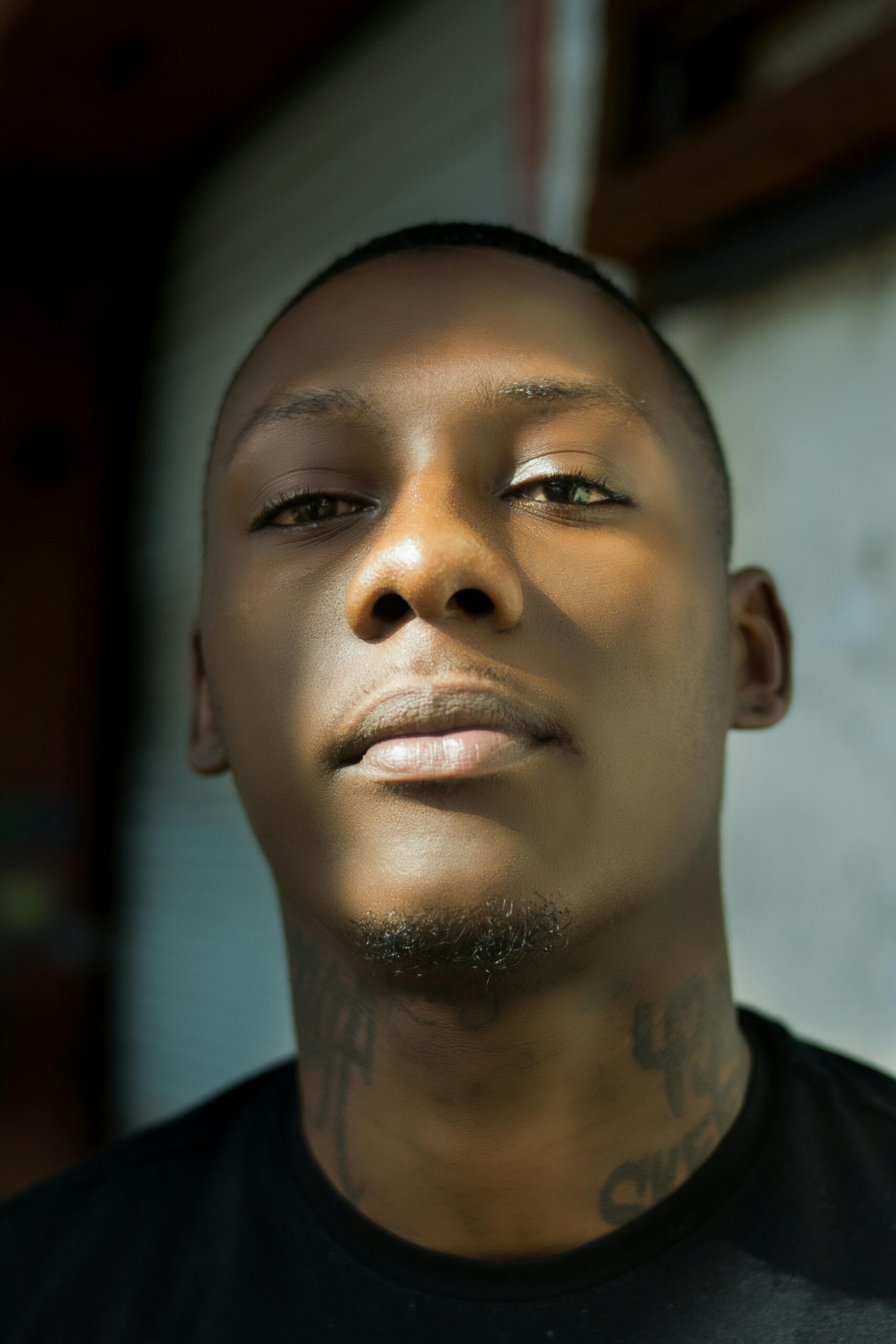 Close-up portrait of a man indoors, showcasing facial tattoos and confident expression.